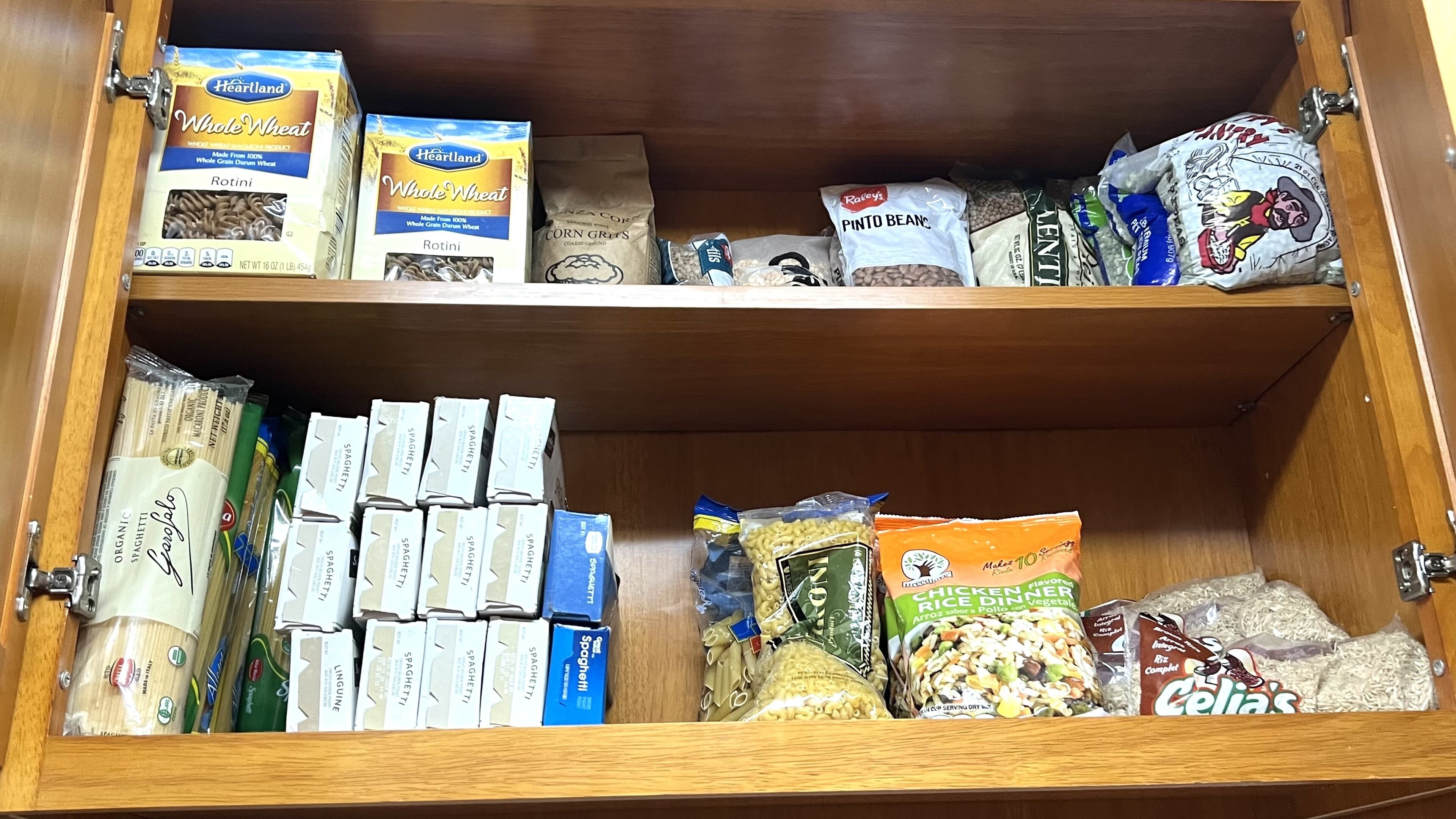 A pantry with various food items including boxes of spaghetti, rotini pasta, and bags of rice.