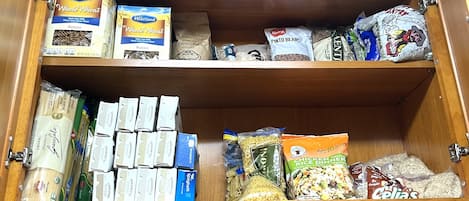 A pantry with various food items including boxes of spaghetti, rotini pasta, and bags of rice.
