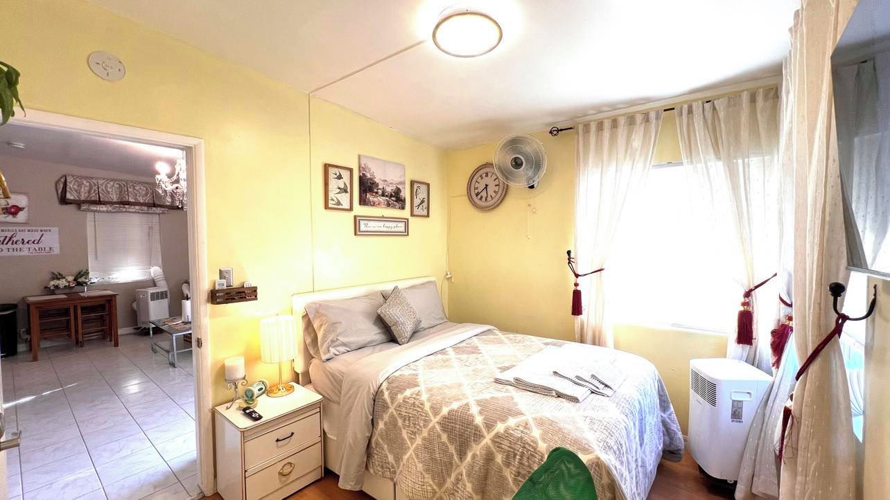 Une chambre à coucher avec un lit, une table de chevet, une lampe et une fenêtre avec des rideaux.