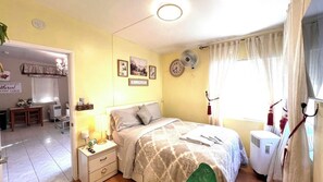 Un dormitorio con cama, mesita de noche, lámpara y ventana con cortinas.
