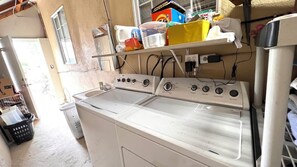 Un lavadero con lavadora y secadora de carga frontal, un estante con productos de limpieza y una ventana.