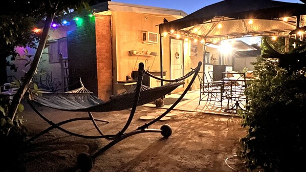Una hamaca bajo una marquesina, un edificio de ladrillo y una tienda de campaña con luces colgantes.