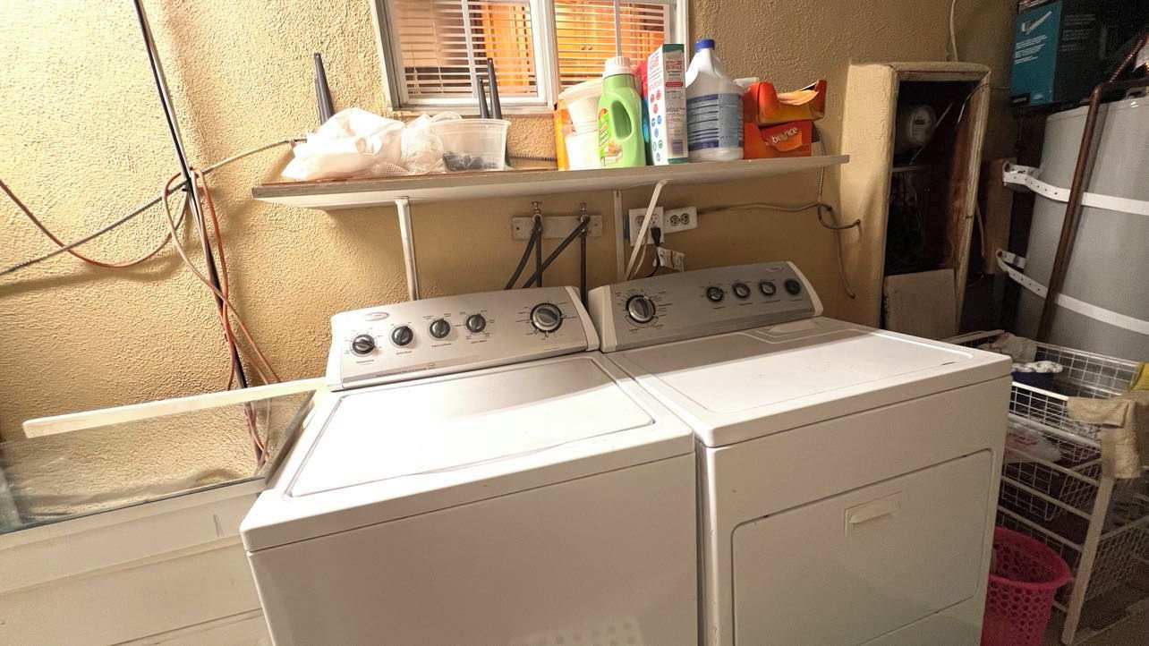 A laundry area with a washer and dryer, a shelf with cleaning supplies, and a window with blinds.