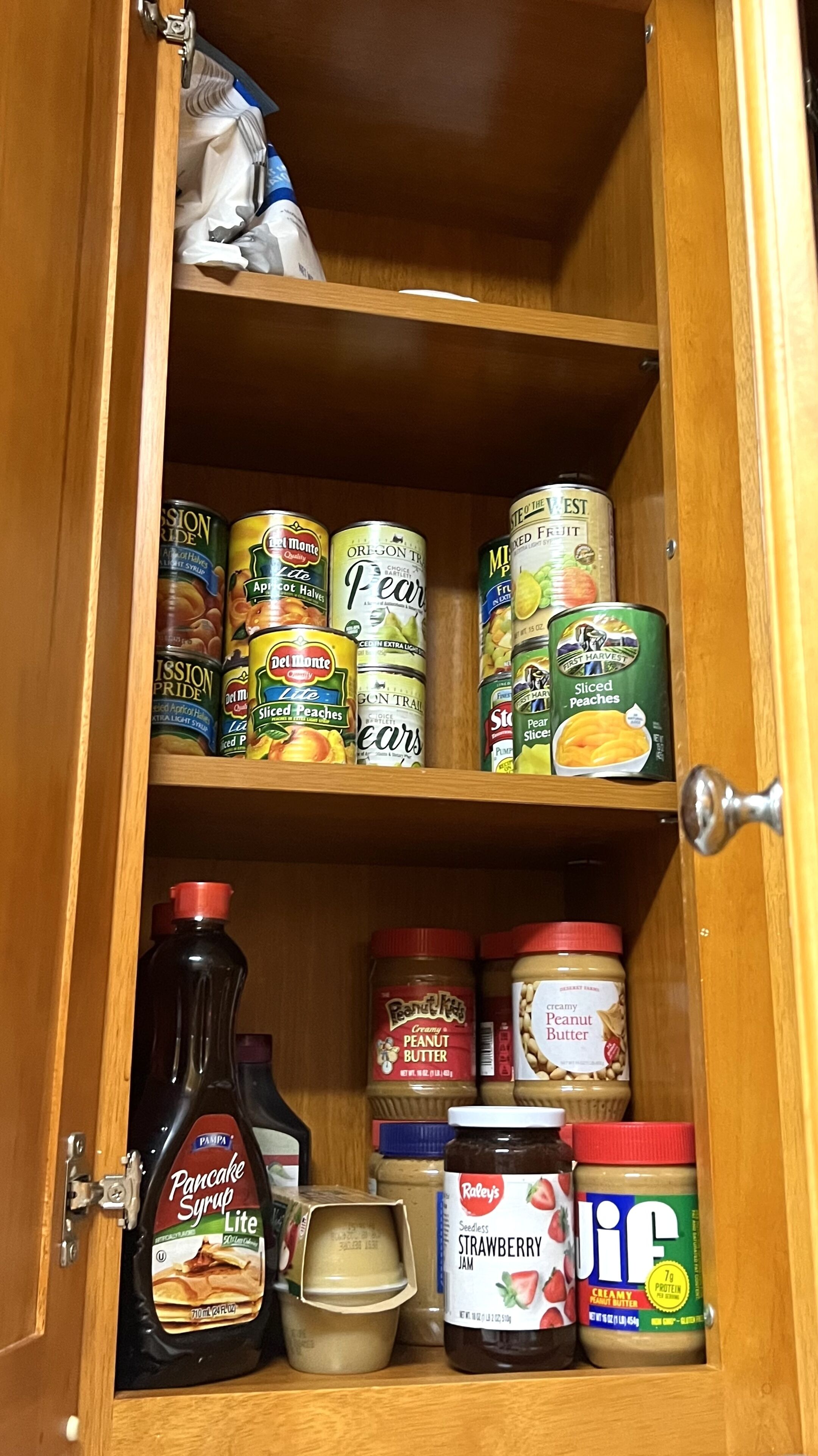A pantry with various food items including canned fruits, peanut butter, and syrup.
