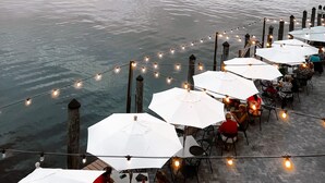 Un restaurante frente al agua con terraza y luces colgantes.