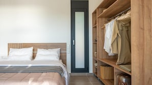 A bedroom with a wooden headboard, a bed with white linens, a wardrobe with hanging clothes, and a door with frosted glass. - Casatino Villas #1 (kalianeika)
