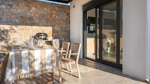 An outdoor dining area with a stone wall, a grill, and a table set for four. - Casatino Villas #1 (kalianeika)