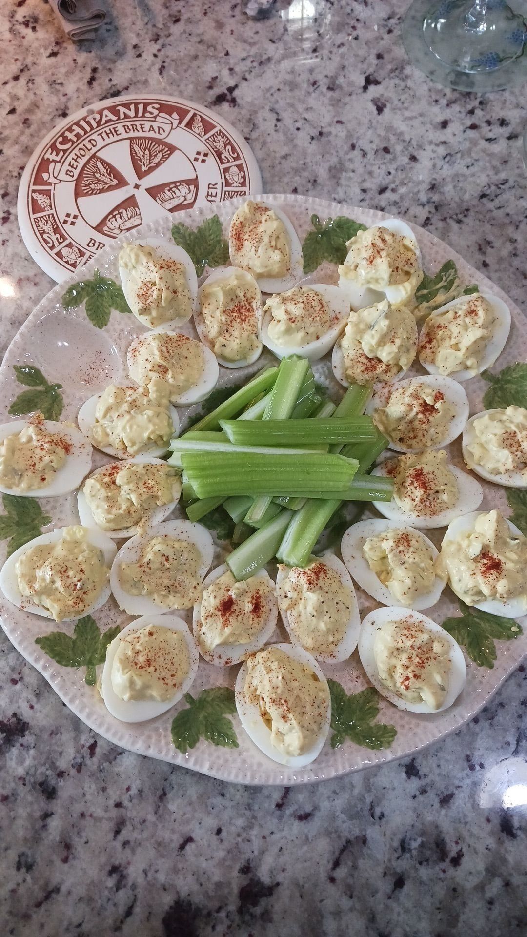 A plate of deviled eggs garnished with paprika and celery sticks, with a bread-themed coaster in the background.