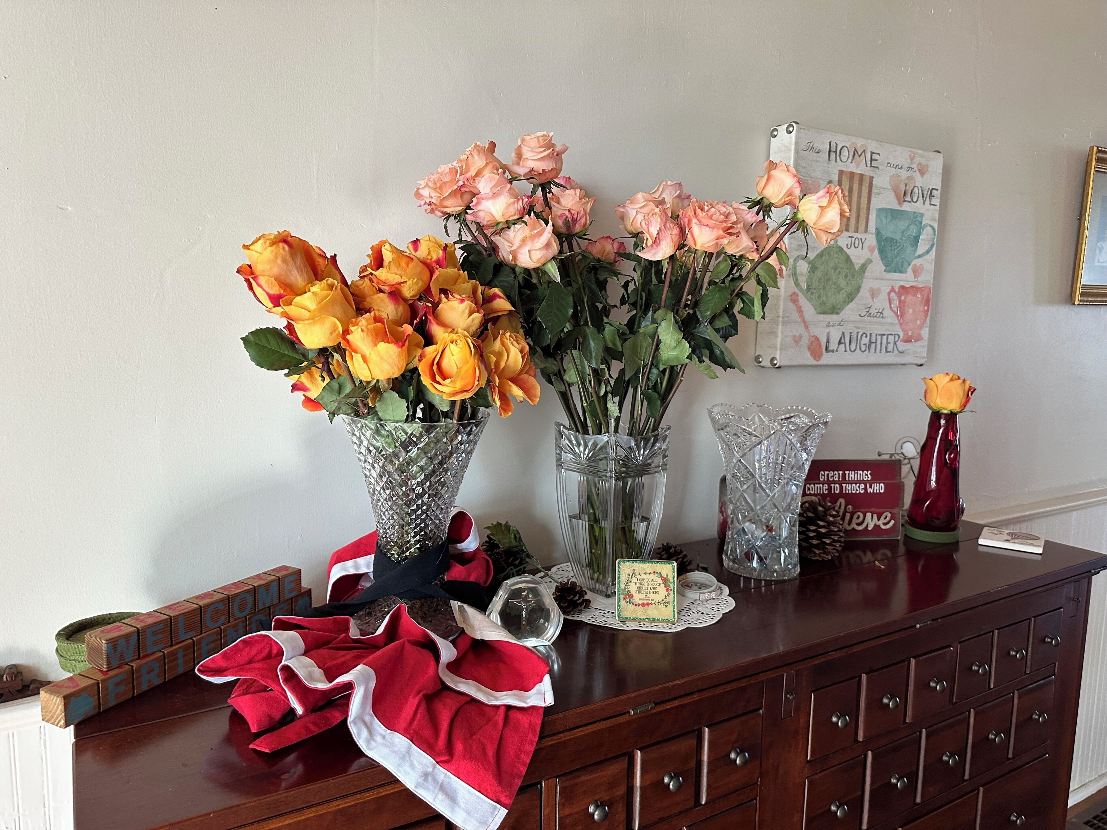 A wooden dresser with two glass vases containing roses, a decorative sign, and a small card.