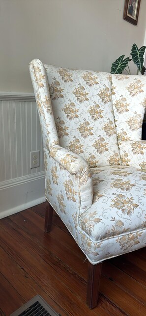A corner of a room with a floral-patterned armchair, a radiator, and a plant.