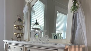 A white dresser with multiple drawers and ornate handles, a large mirror above it, and a decorative item on top.