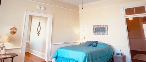 A bedroom with a bed, a nightstand, a lamp, a door with a handle, and a ceiling fan.
