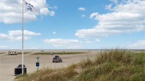 A beach with a flag, a sign, and a car. - Amazing apartment in Fanø with WiFi (Fanø)