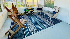 A sunroom with a blue ceiling, a patterned rug, wooden chairs, a small table, and a ceiling fan.