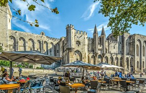 Een terras met tafels en parasols voor een historisch gebouw met bogen en torens.