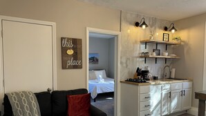 Un espace de vie compact comprenant un coin cuisine, un canapé avec un plaid et un lit à l’arrière-plan.