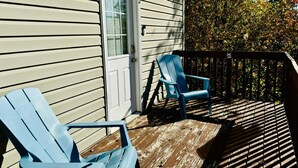 Une terrasse en bois avec deux chaises Adirondack bleues, une porte blanche et une fenêtre avec des volets.