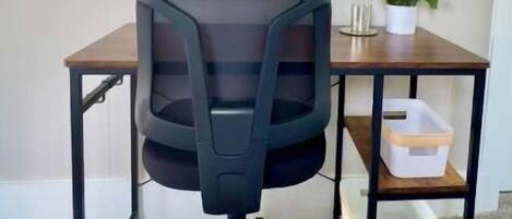 A room with a desk, chair, mirror, potted plant, and storage shelves.