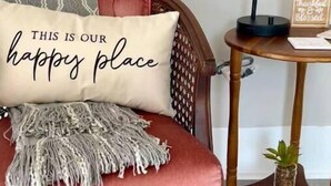 Une pièce chaleureuse avec un canapé rouge, un coussin décoratif, une petite table d’appoint avec une lampe, et une pancarte sur laquelle on peut lire : « Reconnaissant pour toutes les bonnes choses ».