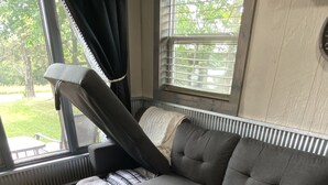 Una sala moderna con un sofá gris, un catre extensible y una ventana con persianas.