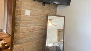 Un baño con pared de madera, un espejo, un televisor sobre el espejo y un balde pequeño.