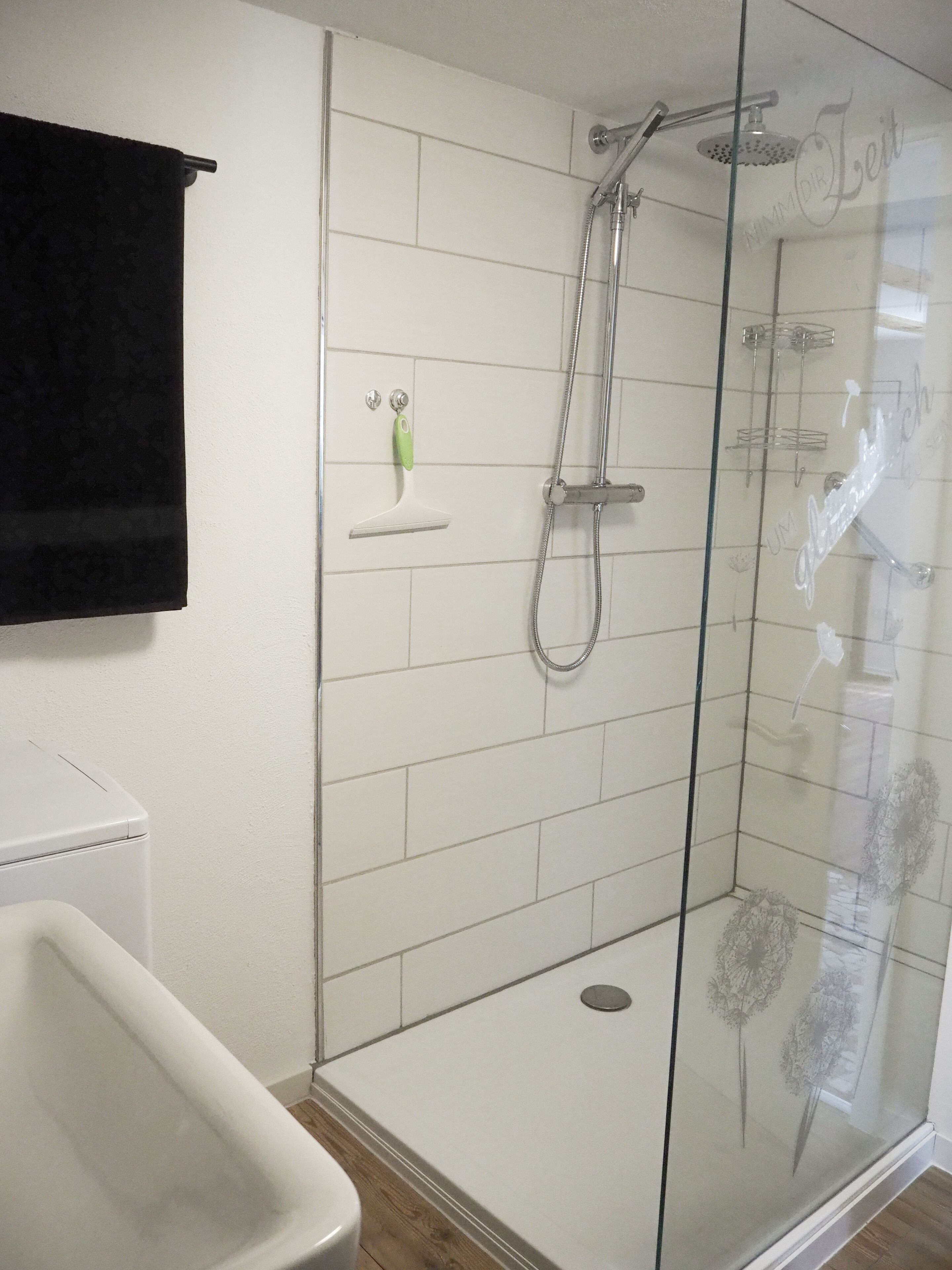 Une douche fermée par des parois en verre, dotée d’un pommeau de douche à main et d’un robinet mural.