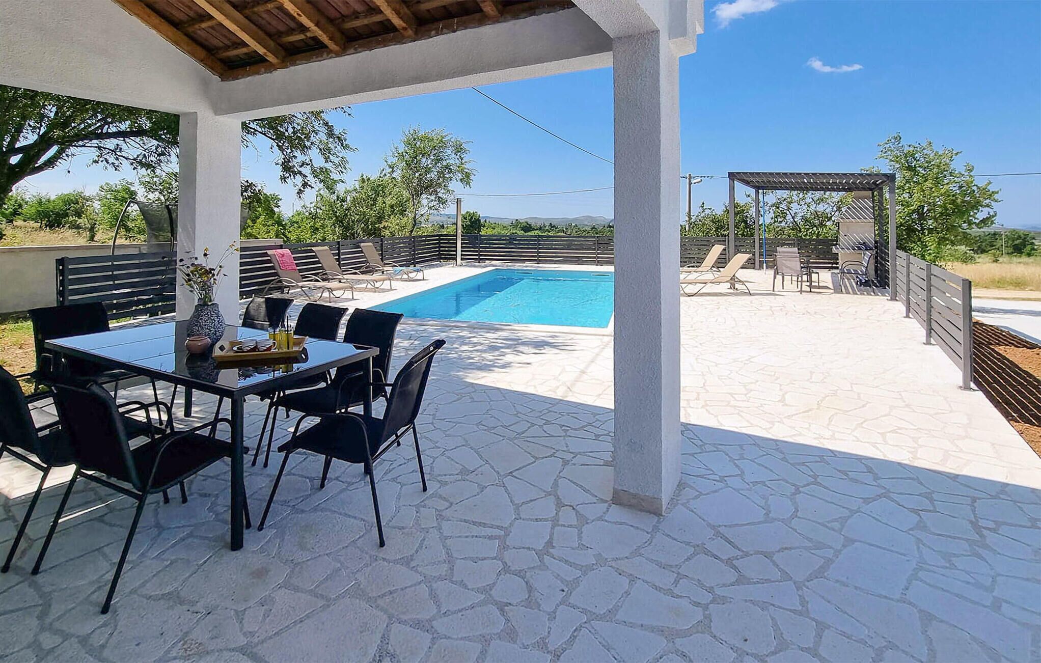 Ein Poolbereich im Freien mit überdachter Terrasse, Steinböden und Liegestühlen.