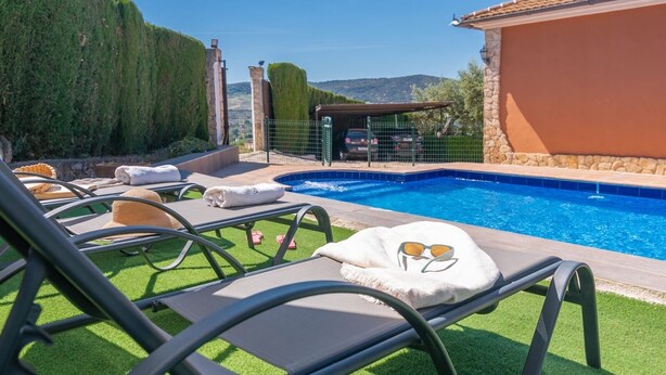 A pool area with lounge chairs, a stone wall, and a view of the landscape. - Bellavista Arriate by Ruralidays (Málaga)