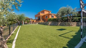 A well-maintained lawn with a basketball hoop, a stone wall, and a two-story building in the background. - Bellavista Arriate by Ruralidays (Málaga)