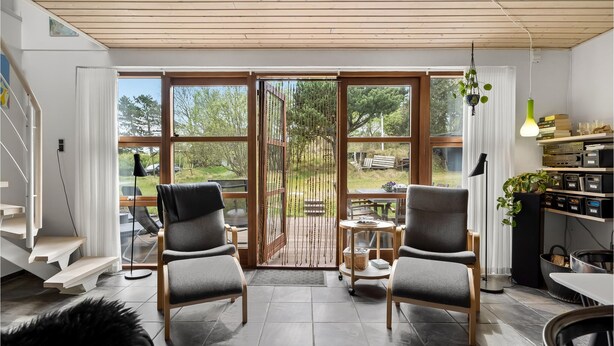En moderne stue med to grå lænestole, en trætrappe og et spiseområde med bord og stole.