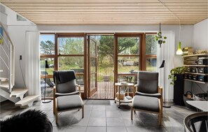 Un salon moderne avec deux fauteuils gris, un escalier en bois et un coin repas comprenant une table et des chaises.