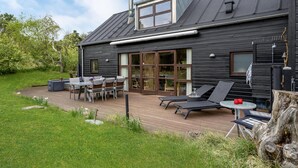 Et moderne træhus med terrasse, udendørs møbler og store vinduer.