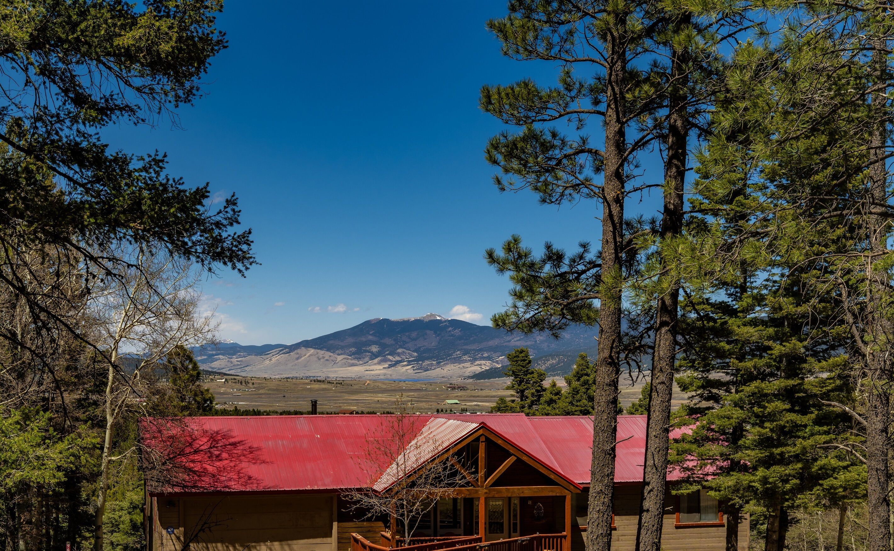 Una cabaña de techo rojo, rodeada de altos pinos, con vistas a una cadena montañosa.