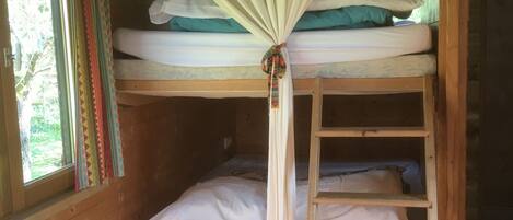 A bunk bed with a canopy, a ladder, and a window with curtains.