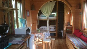 Een gezellig interieur van een chalet met een eethoek, stapelbedden en een kleine keukenhoek.