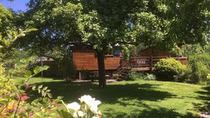 Een houten chalet met een overdekte veranda, omringd door weelderige begroeiing en bloeiende planten.