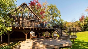 Eine Holzterrasse mit Adirondack-Stühlen, einer Treppe und Blick auf ein Haus mit Balkon.