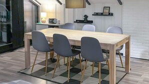 A modern dining area with a wooden table, four grey chairs, a patterned rug, a television on the wall, and a shelf with a picture frame. - Stunning home in Rødby with kitchen (Rødby)