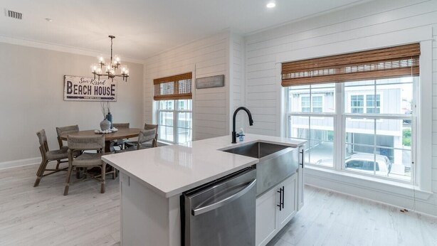 A modern kitchen with a central island, white cabinetry, and a large window with blinds. - Sun-Kissed at Summer Salt (Orange Beach)
