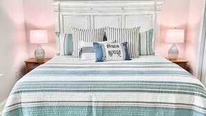 A bedroom with a large bed, two bedside lamps, a headboard with a decorative panel, and two framed wall art pieces above the bed. - Sun-Kissed at Summer Salt (Orange Beach)