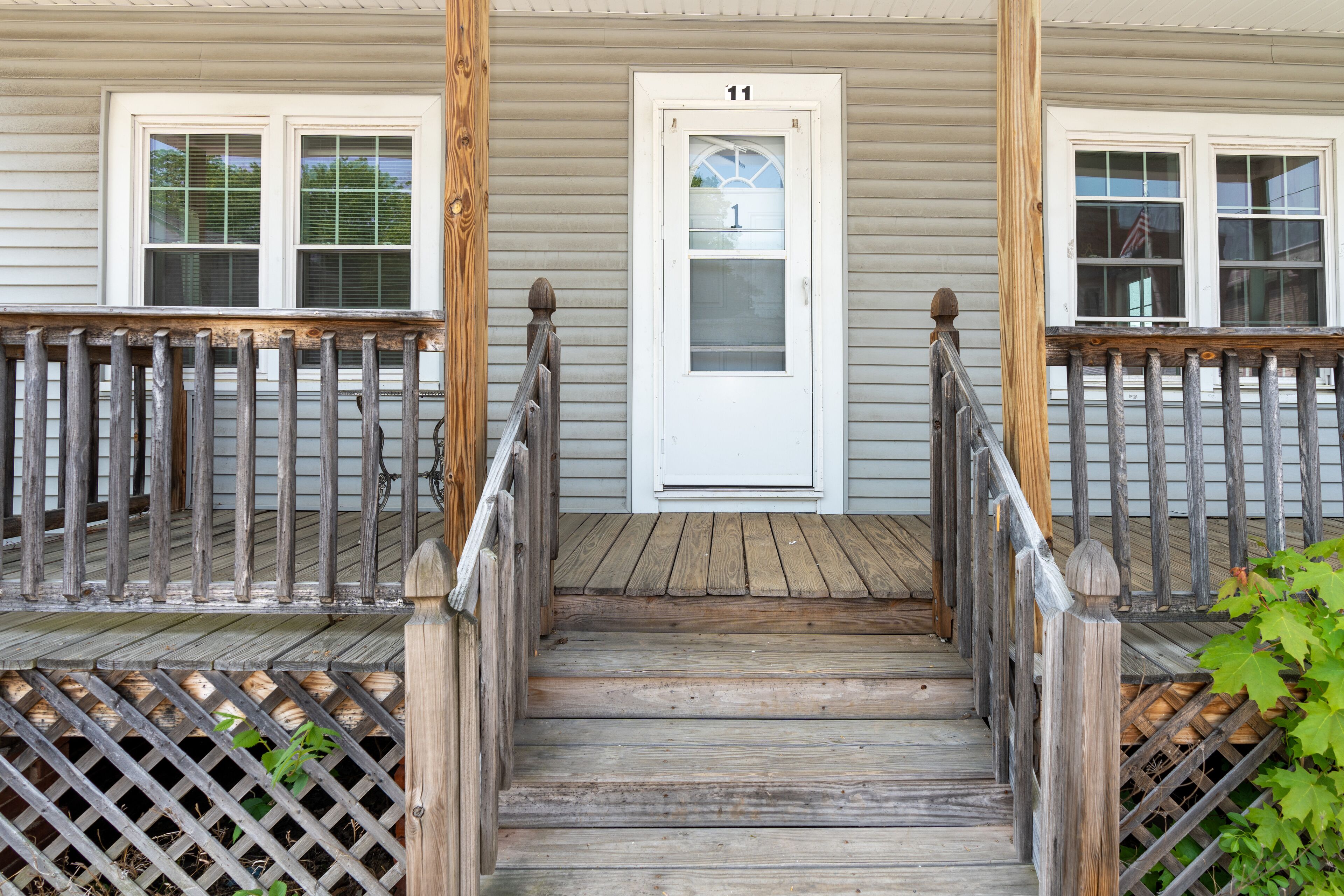 A wooden front porch with a white door marked '11', a wooden staircase, and a wooden railing.