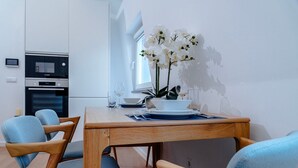 Un comedor con una mesa de madera, sillas azules, flores de orquídea blanca y una cocina moderna al fondo.