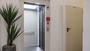 Un ascensor con un letrero rojo de salida de emergencia, una planta en maceta y una puerta con manija.