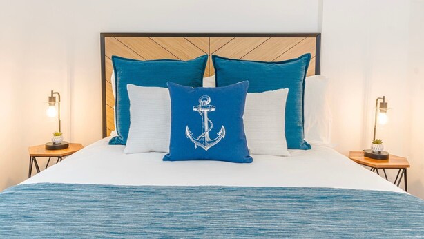 Una cama con cabecera de madera, dos mesitas de noche y una almohada con forma de ancla azul.