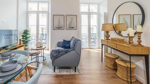 Una sala de estar moderna con un sofá gris, una mesa de comedor con platos y cubiertos, un televisor y un balcón con vistas.