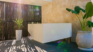 A reception area with a modern reception desk, a stone wall, and potted plants. - Fabulous Apartment With Private Pool · 306 (Tulum)