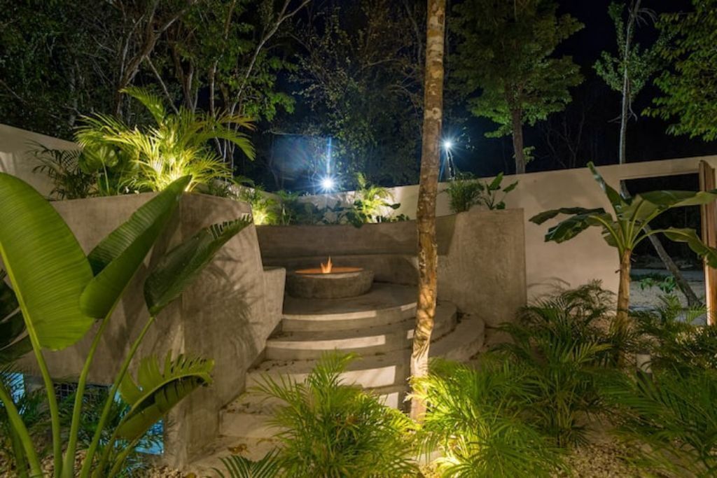 Un espace extérieur aménagé pour la nuit, comprenant un foyer, des marches et une végétation environnante.