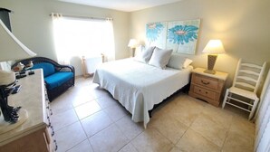 Une chambre à coucher comprenant un lit, des tables de chevet, une chaise, une commode et des œuvres d’art accrochées au mur.