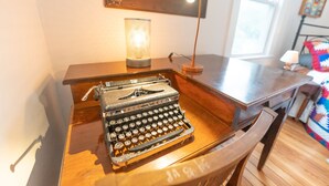 A vintage typewriter on a wooden desk with a lamp and a framed artwork on the wall. - Vintage Space! 60 Seconds from Downtown Lee Summit (Lee's Summit)