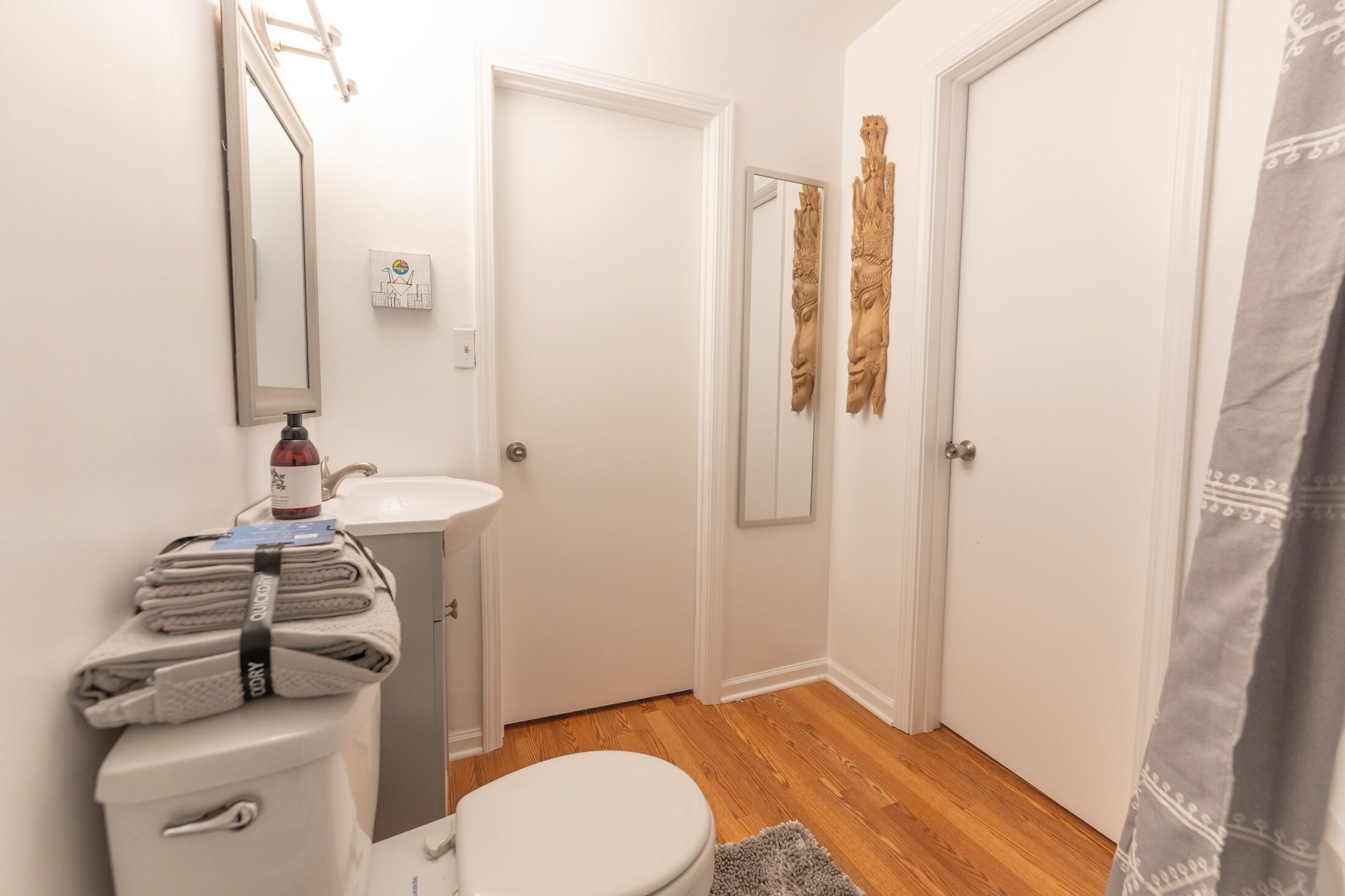 A bathroom with a toilet, sink, and mirror. There is a towel rack with folded towels and a bottle on the sink.